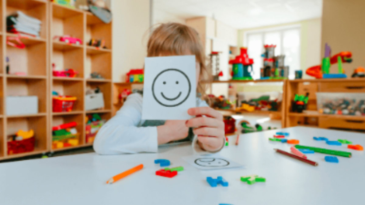 Criança em ambiente terapêutico segurando uma imagem com rosto sorridente durante avaliação psicológica, representando atendimento neuropsicológico infantil em ambiente lúdico.