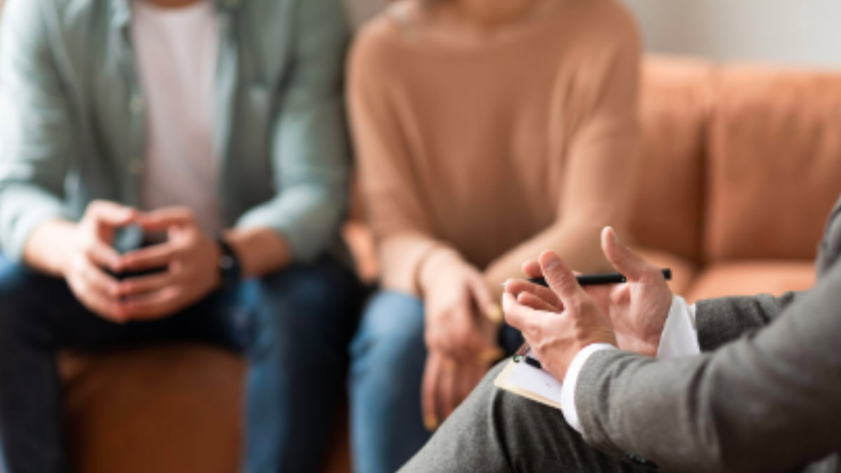 Casal em consulta com psicólogo, sentado em um sofá, em ambiente acolhedor.
